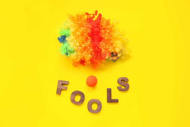 Composition with clown wig, nose and word FOOLS on yellow background - Photo, Image