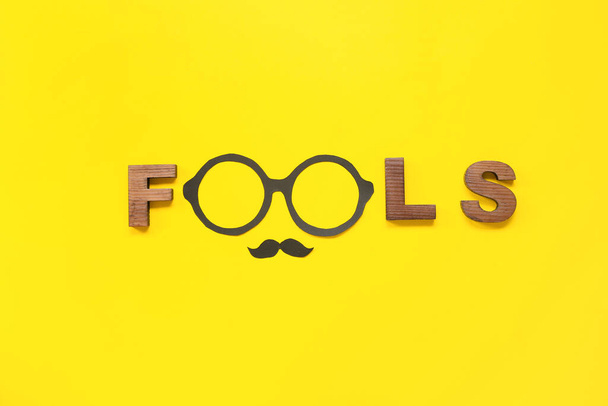 Word FOOLS and party decor on yellow background. April Fools Day celebration - Foto, Imagen