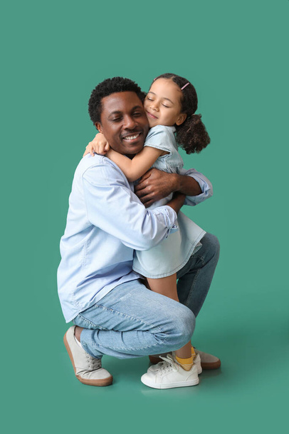Porträt eines kleinen afroamerikanischen Mädchens, das seinen Vater auf grünem Hintergrund umarmt - Foto, Bild