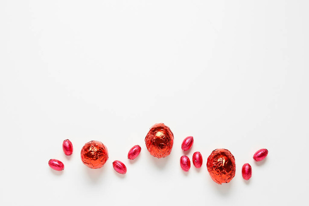 Шоколадные пасхальные яйца, завернутые в красную фольгу на белом фоне - Фото, изображение