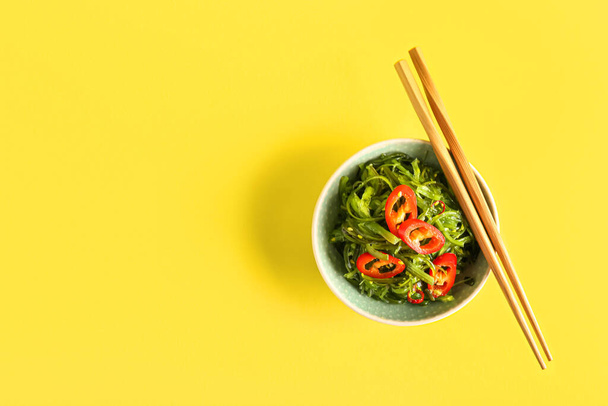 Bowl with healthy seaweed salad and chili pepper on yellow background - Photo, image