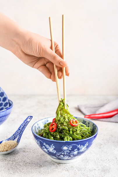 女性は明るい背景に箸で健康的な海藻サラダを食べる - 写真・画像