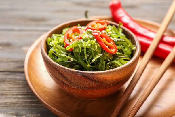 Bowl with healthy seaweed salad and chili pepper on light wooden background, closeup - 写真・画像