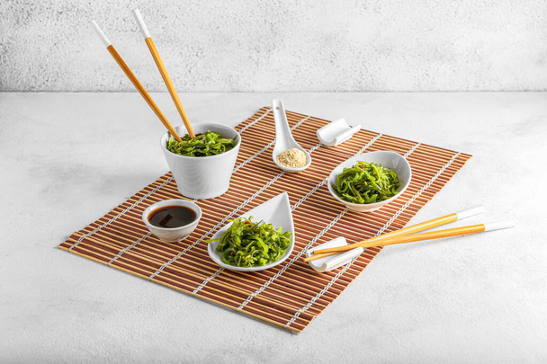 Bowls with healthy seaweed salad, sauce and sesame on light background - Photo, Image