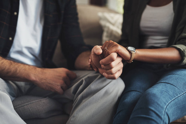 Hand in hand through it all. Shot of an unrecognizable couple holding hands while sitting on a sofa at home. - Photo, Image