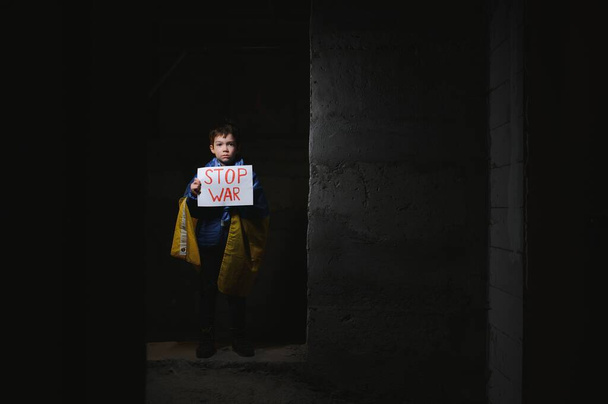 Portrait sad boy protesting war raises banner with inscription Stop War at blue yellow flag of country Ukraine. Call to stop war, child against war, crisis in Ukraine. - Foto, Imagen