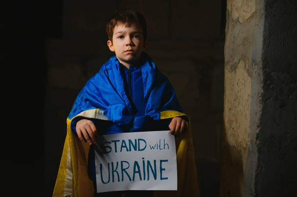 Upset Ukrainian poor toddler boy kid homeless protesting war conflict raises banner with inscription massage text No War on black background. Crisis, peace, stop aggression, child against Russian war - Zdjęcie, obraz