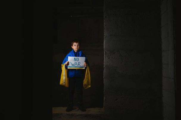 Upset Ukrainian poor toddler boy kid homeless protesting war conflict raises banner with inscription massage text No War on black background. Crisis, peace, stop aggression, child against Russian war - Foto, Imagen