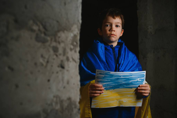 Ukrainian Crying boy holds a painted flag of Ukraine. War of Russia against Ukraine. Ukrainian Crying boy asks to stop the war in Ukraine. Child with message Stop War. - Φωτογραφία, εικόνα