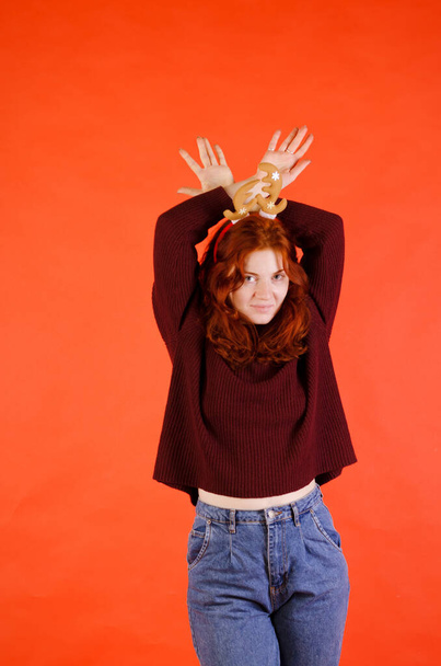 Porträt einer schönen jungen Frau, Mädchen mit roten lockigen Haaren und blauen Augen im Pullover vor rotem Hintergrund. Hirschhörner auf dem Kopf. Neujahr, Weihnachtsfeier. - Foto, Bild