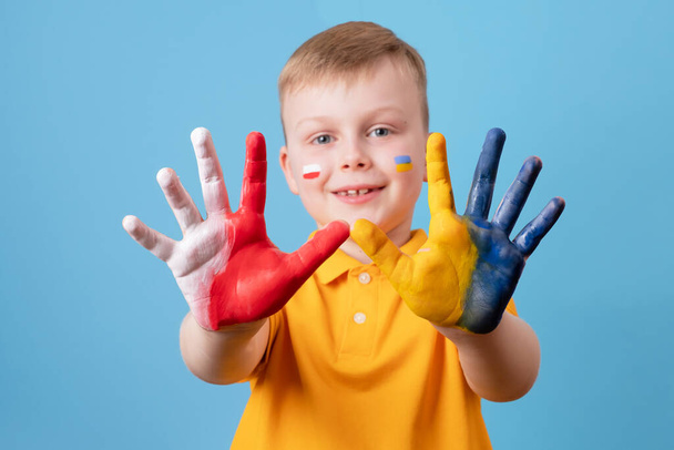 ウクライナとポーランドの国旗の色で描かれた子供の手。青い背景に隔離されています。ウクライナ人のためのポーランド人の慈善援助。高品質の写真 - 写真・画像