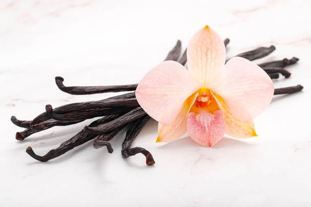 Getrocknete Vanillestäbchen und Orchideenblume auf Marmorhintergrund. - Foto, Bild