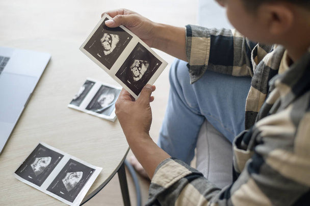 Young father holding ultrasound photo of newborn baby, maternity and family concept - Foto, Imagen