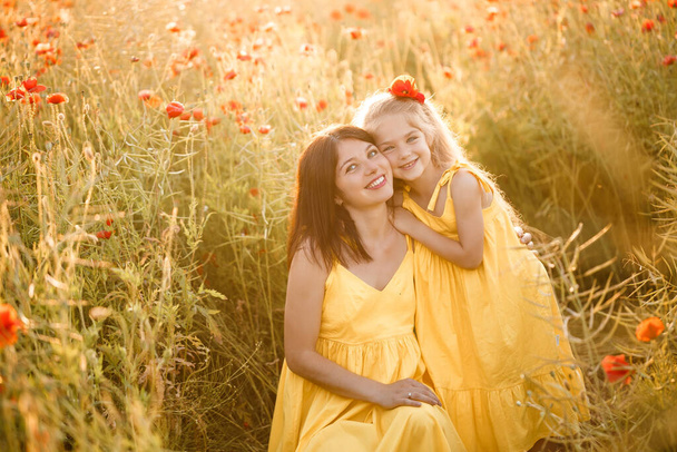 Een jonge zwangere vrouw met haar dochter in gele jurken staan in een papaverveld. Familierelaties - Foto, afbeelding
