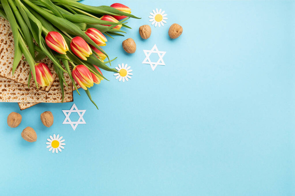 Żydowskie święto Pozdrowienia z okazji Święta Paschy koncepcja kartki z macy, orzechy, stokrotki i kwiaty tulipan na niebieskim stole. Seder Pesach wiosna wakacje tło, widok z góry, przestrzeń do kopiowania. - Zdjęcie, obraz