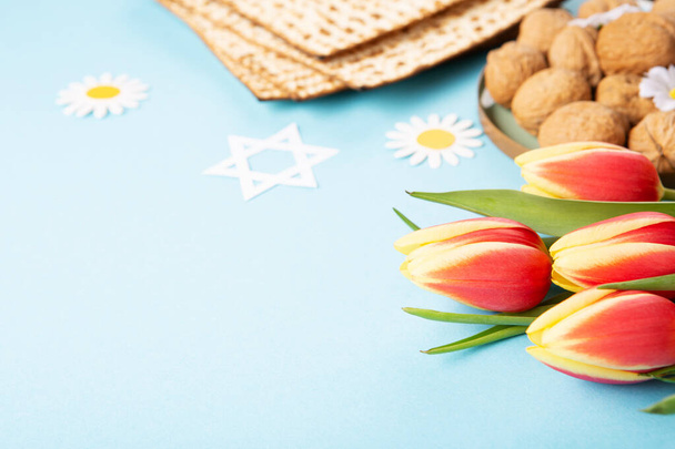 Yahudi bayramı tebrik kartı konsepti, matza, fındık ve lale çiçekli mavi masa. Seder Pesach bahar tatili arka planı, kopyalama alanı. - Fotoğraf, Görsel