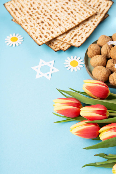 Fiesta judía concepto de tarjeta de felicitación Pascua con matzá, frutos secos y flores de tulipán en la mesa azul. Seder Pesaj fondo de vacaciones de primavera, espacio de copia. - Foto, imagen