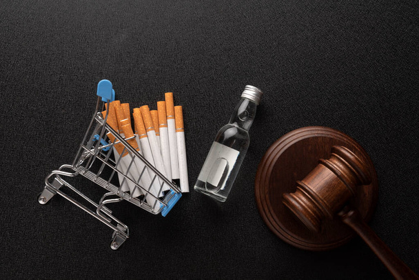 Az alkohol és a dohány adásvételi törvényének megsértése. Bíró úr, fából készült kalapács, cigaretta és egy üveg alkohol. Felülnézet - Fotó, kép