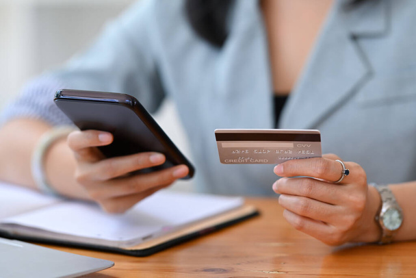 Kapalı görüşlü genç bir kadın kredi kartı tutuyor ve online bankacılık veya akıllı telefonuyla ödeme yapıyor.. - Fotoğraf, Görsel