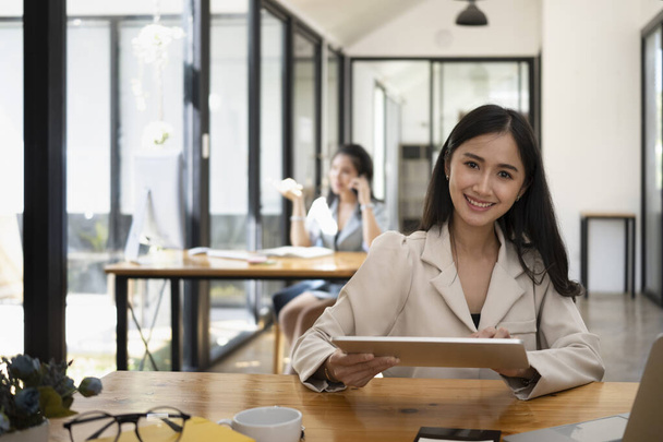 Sonriente hermosa asesora financiera femenina sentada en el lugar de trabajo moderno y el uso de tabletas digitales. - Foto, imagen