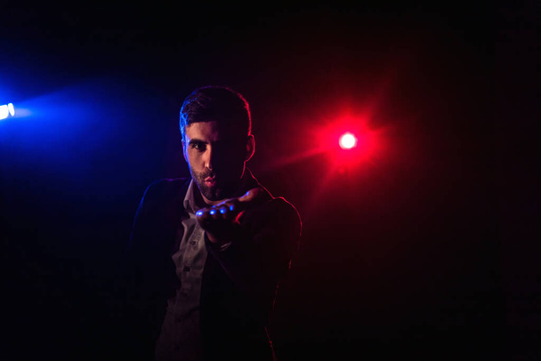 Photo of man looking at camera on dark background with pink and blue lights. - Photo, Image