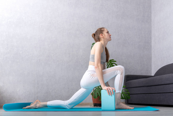 Chica hace ejercicio de estiramiento en estera de yoga con ladrillos de espuma. Yoga y gimnasia en casa. Ejercicio para principiantes. - Foto, Imagen