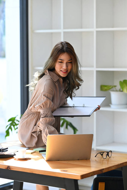 Charming young asian woman entrepreneur sitting on her office desk and using laptop. - Photo, Image