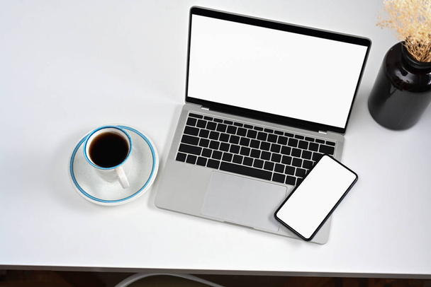 Mockup laptop, smartfon i filiżanka kawy na białym stole. - Zdjęcie, obraz