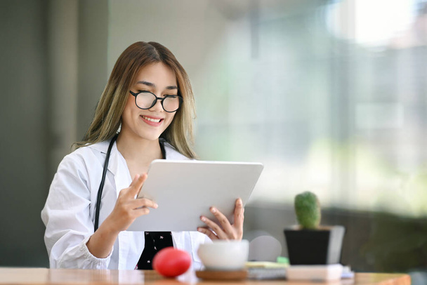 Χαμογελώντας γυναίκα γιατρός χρησιμοποιώντας ψηφιακή ταμπλέτα στο φωτεινό σύγχρονο νοσοκομείο. - Φωτογραφία, εικόνα