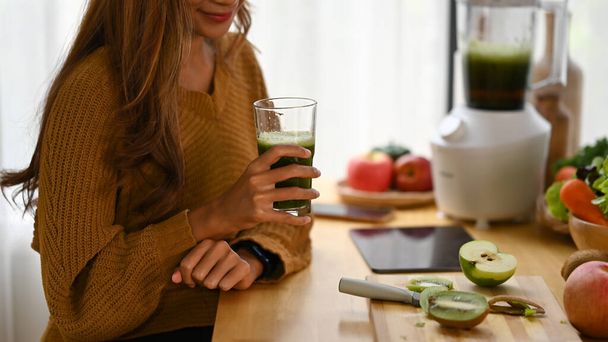 Uśmiechnięta kobieta pijąca zielony koktajl warzywny detox w domu. Koncepcja zdrowego stylu życia. - Zdjęcie, obraz