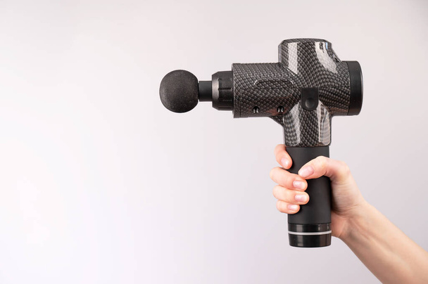 Close-up of a female hand with a portable massager gun on a white background.  - Foto, Imagen