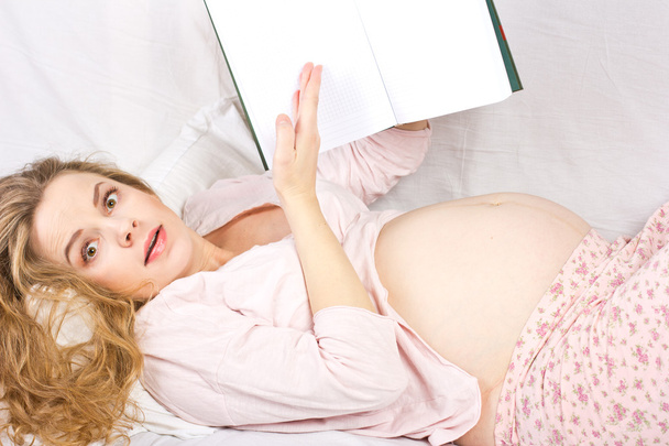 Beautiful pregnant blonde reading a book in bed. Portrait of pregnant woman - Photo, Image