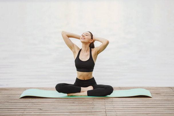 Woman practicing advanced yoga by the water - Photo, image