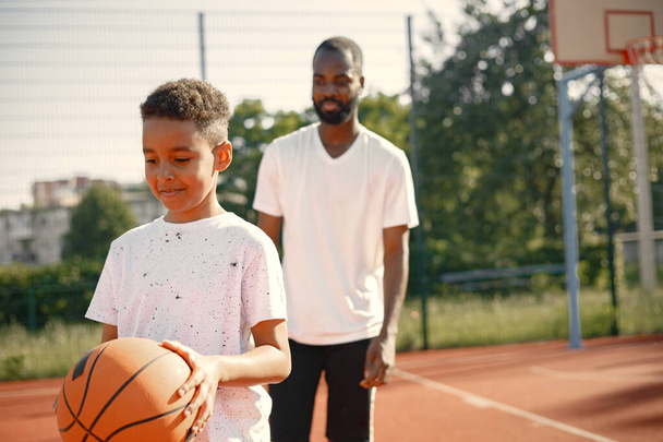 Black father with son playing basketball in basketball court together - Fotoğraf, Görsel