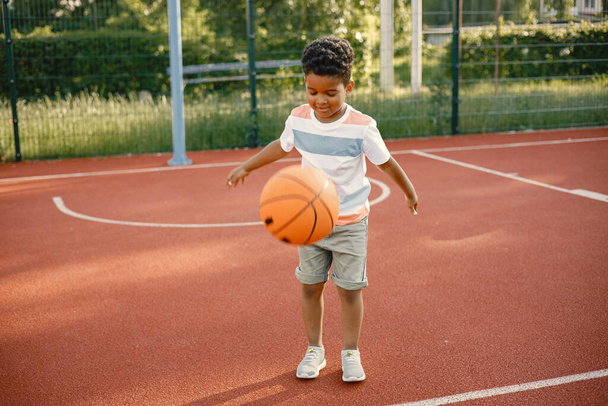 Multiracial boy standing on a basketball court and play with an orange ball - Zdjęcie, obraz