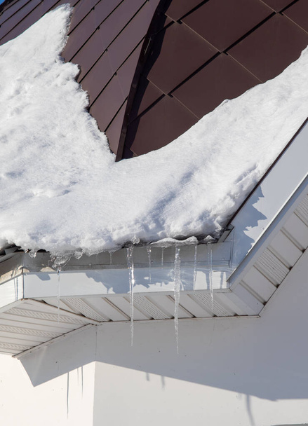 Ice icicles and snow hang from the roofs of houses. - Φωτογραφία, εικόνα
