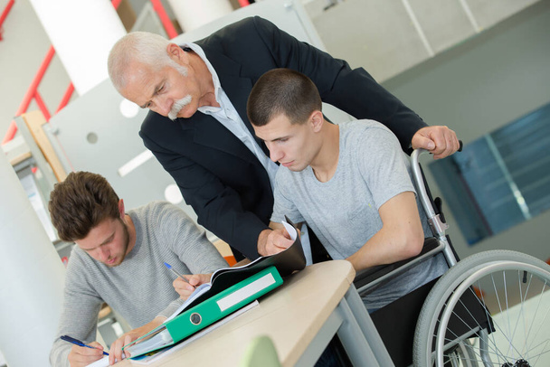 Teacher looking over students' shoulder, one in wheelchair - Fotografie, Obrázek