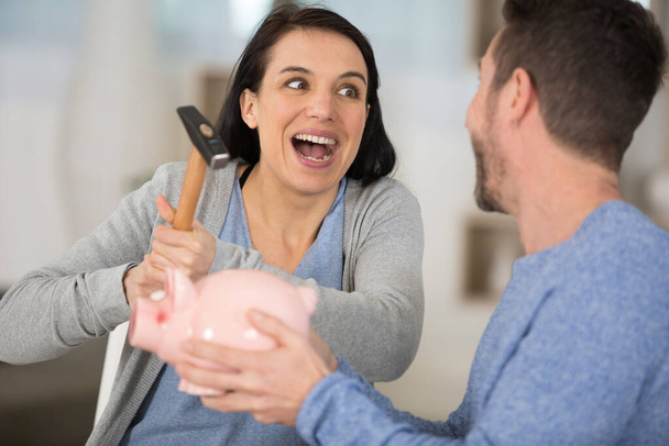young couple breaking piggy bank with hammer at home - Foto, Bild