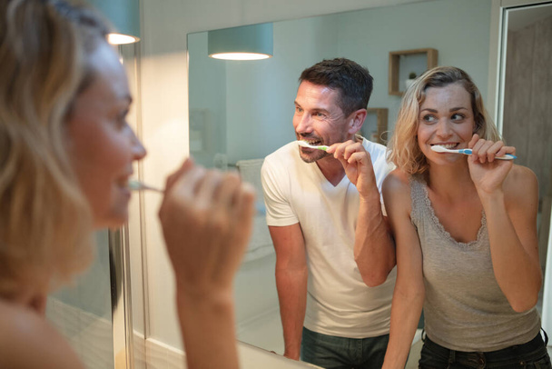 smiling man and woman brushing teeth in bathroom - Foto, afbeelding