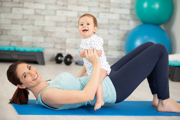 young mother does physical fitness exercises together with her baby - Foto, afbeelding