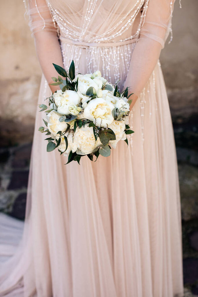 The bride in a pastel dress holds a beautiful wedding bouquet of white peonies - Foto, Imagen