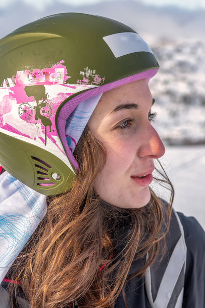 Ženy s hnědou pletí stojící na vrcholu hory, oblečené v lyžařské helmě a lyžařském oblečení, vážný výraz obličeje, pohled na sjezdovku, stryn norway zblízka, vertikální - Fotografie, Obrázek