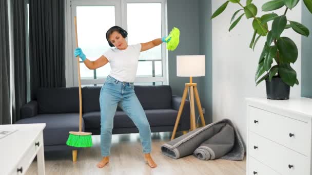 Donna in cuffia pulire la casa e divertirsi ballando con una scopa e un panno. Rallentatore - Filmati, video