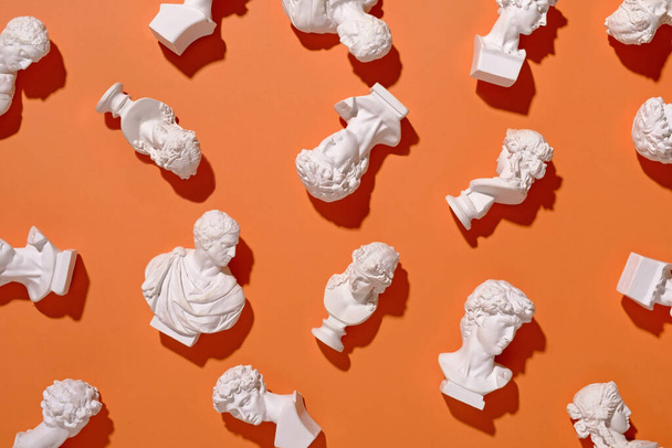 Assorted scattered small white busts in antique Roman style on an orange background in a flat lay overhead view - Fotoğraf, Görsel