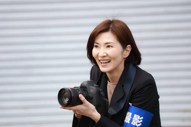 Képek egy női fotósról, aki karszalagot visel, és a karjára van írva a "lövés" szó japánul. - Fotó, kép