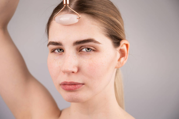 Close-up portrait of a woman uses a quartz roller massager to smooth wrinkles on her forehead. - Foto, Imagem