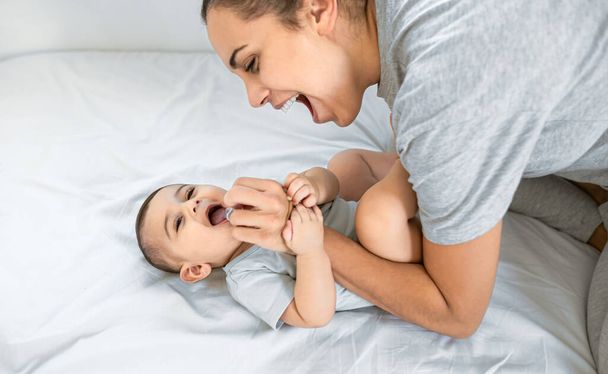幸せな母親はベッドの上で彼女の小さな赤ちゃんと楽しみを持っています-家族と妊産婦の概念 - 写真・画像