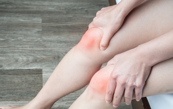 Primo piano delle mani delle donne che si stringono e massaggiano il ginocchio, soffrendo di dolore al ginocchio. Il dolore al ginocchio può essere il risultato di una lesione, come una rottura del legamento o lacerazione della cartilagine. - Foto, immagini