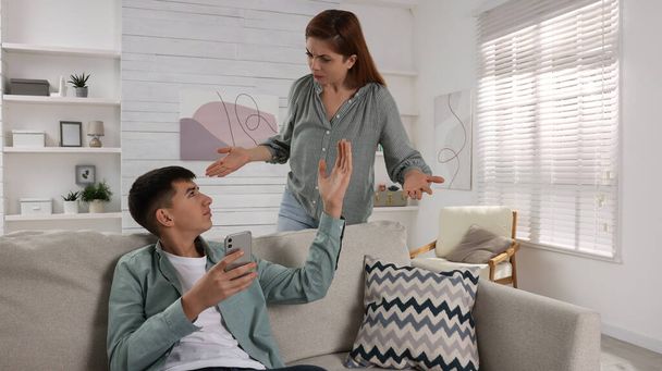 Mother scolding her son while he using smartphone at home. Teenager problems - Zdjęcie, obraz