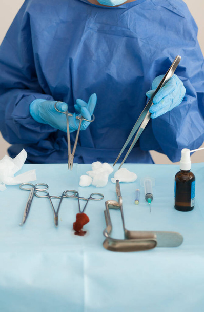 Instruments de curetage stériles, pinces, rétracteur dans la salle d'opération d'un hôpital médical pour le traitement de l'avortement, des règles féminines anormales ou des saignements. Docteur, vêtements spéciaux - Photo, image